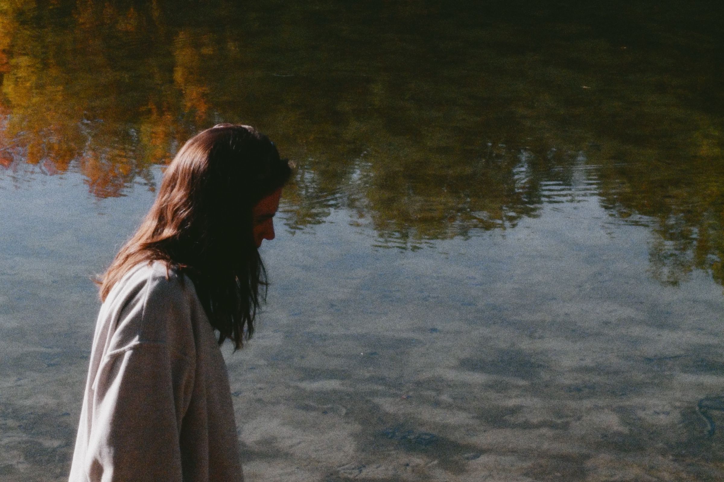 Mujer mirando el reflejo de árboles en el agua