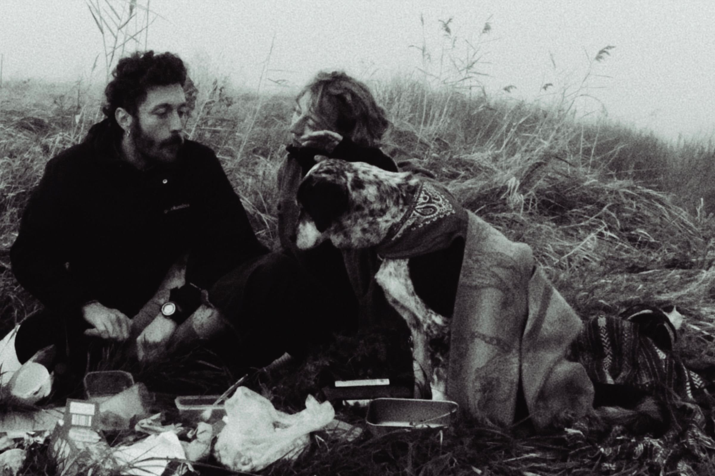Dos personas y un perro sentados en un campo