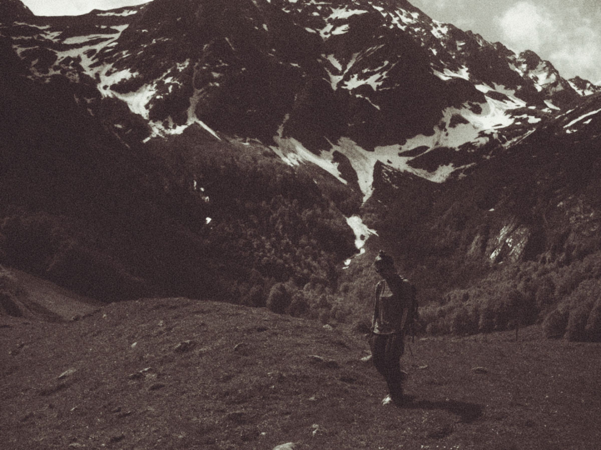 Persona caminando frente a una montaña nevada, tono sepia